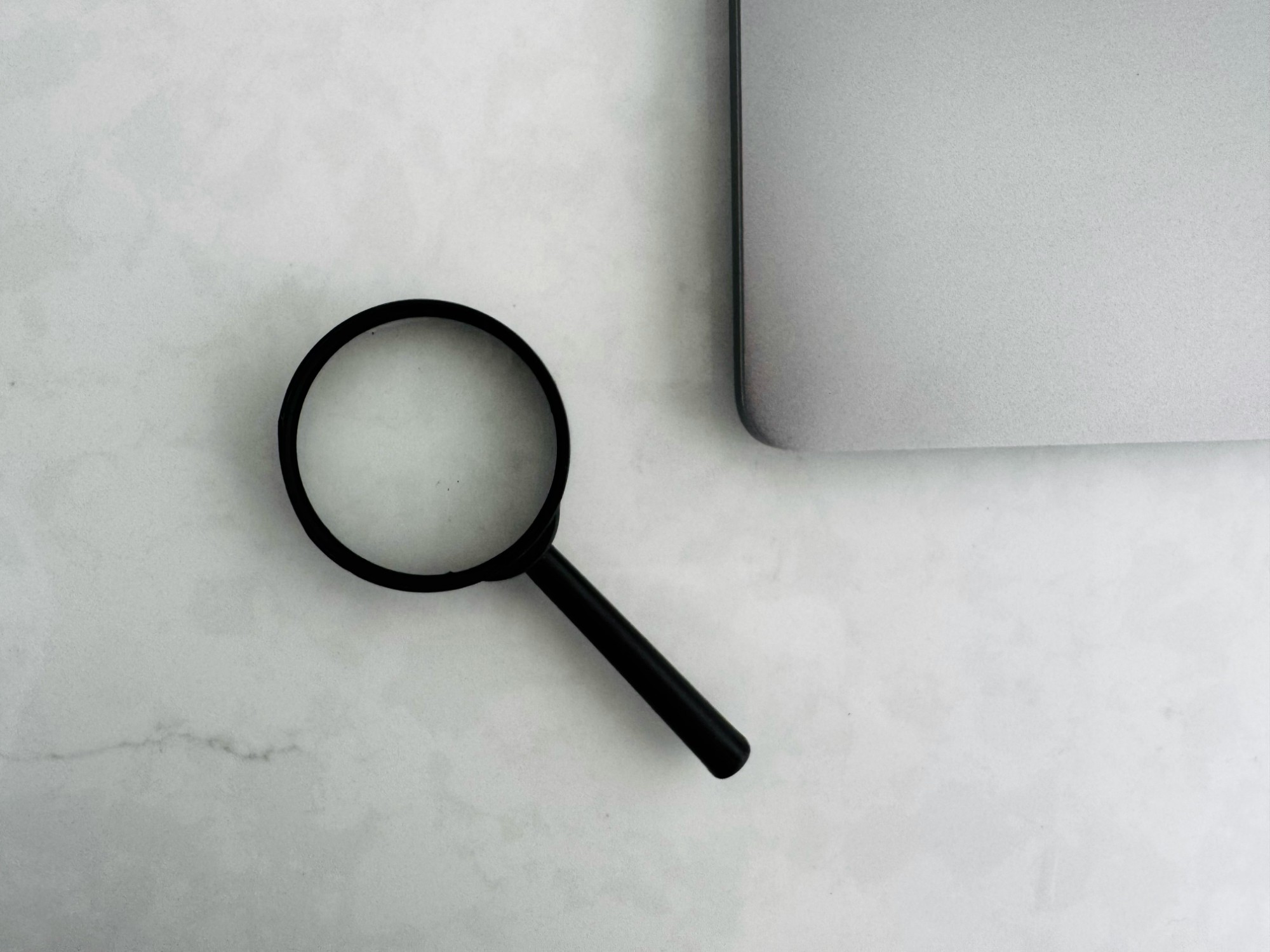 Lupa preta sobre uma mesa de mármore claro, ao lado do canto de um notebook